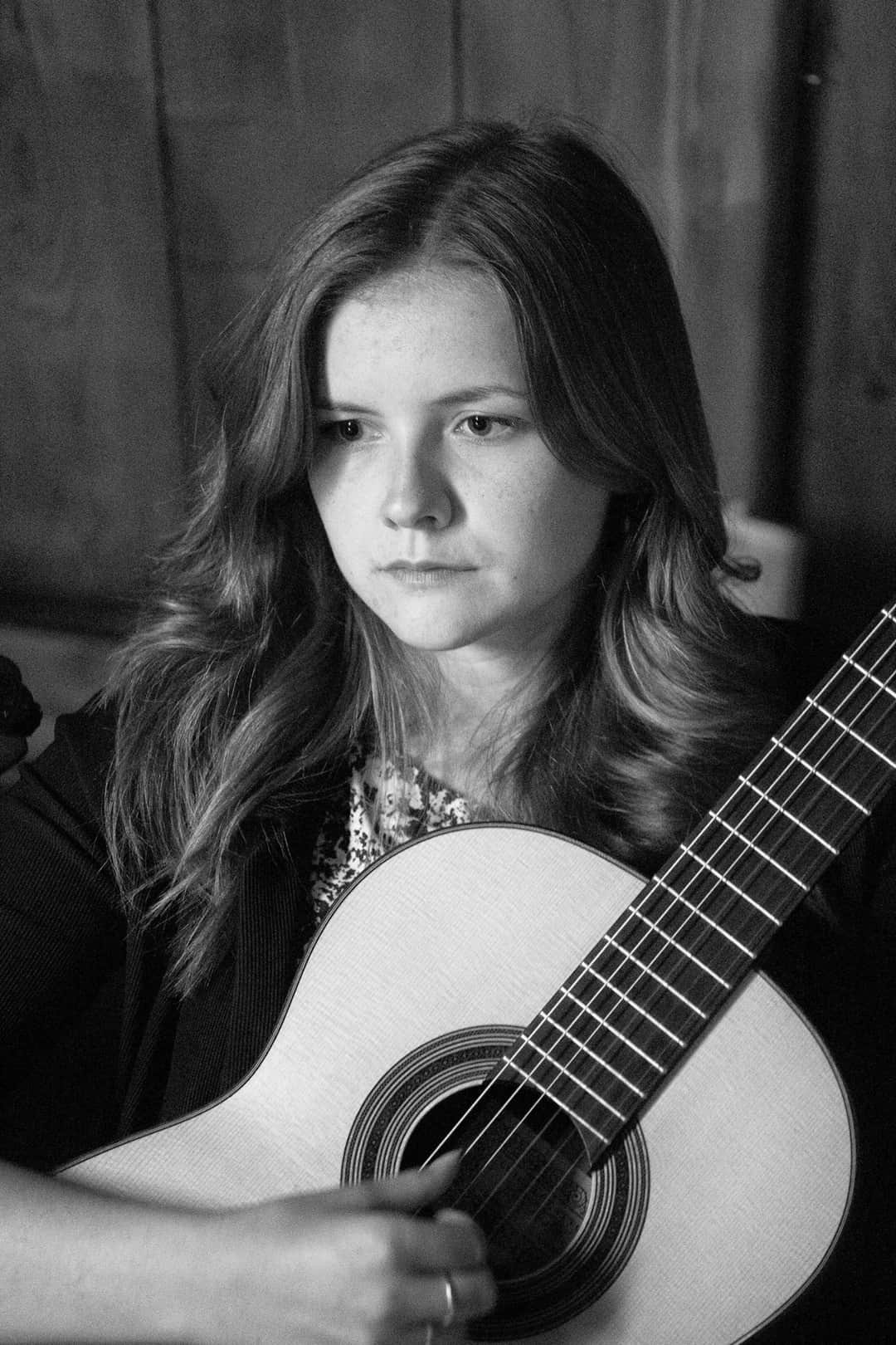 Maria Korzeniowska z gitarą klasyczną na ciemnym portrecie scenicznym